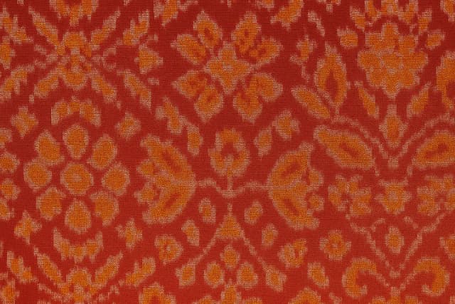 A detailed close-up of authentic Patola fabric showcasing fine double ikat weaving in red and gold with geometric floral motifs.